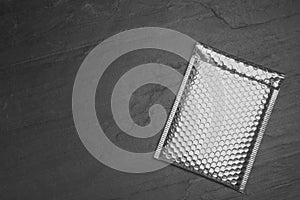 Padded envelope with bubble wrap on black background, top view. Space for text photo