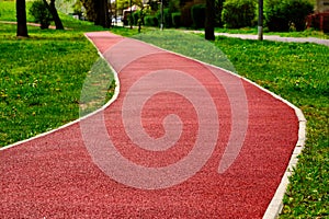 padded red rubber sport and running track floor. soft granular safety flooring. lush green park