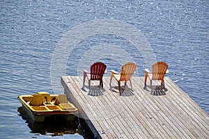 Paddle boat and row of red and yellow Muskoka chairs casting shadows on dock at Spring Lake