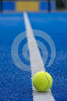 A paddle tennis ball in the foreground on the line of a blue paddle tennis court, racket sports concept