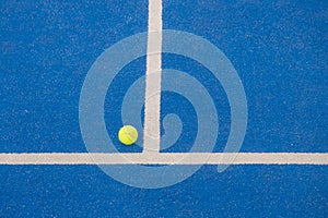 paddle tennis ball next to the baseline of a blue paddle tennis court