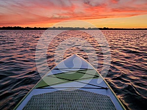 Paddleboard floating on the water with the colorful light of sunset reflecting off the waves at dusk