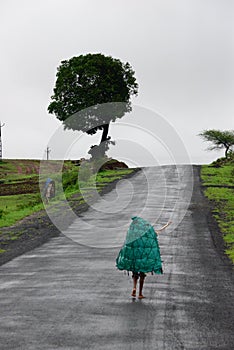 Paddy worker walking on a wet road on a gloomy day