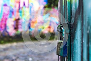 padlock closes a green iron gate with multicolored art concept in blurred graffiti