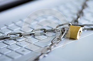Padlock with metal chain hooked and locked across computer keyboard, internet security concept