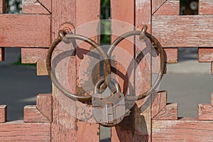 Padlock and metal rings on weathered painted vintage wooden gates.