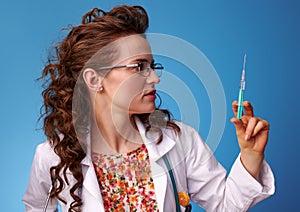 Paediatrician woman looking at syringe on blue