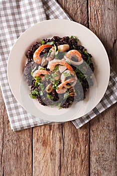 Paella from black rice with seafood close-up on a plate. Vertical top view