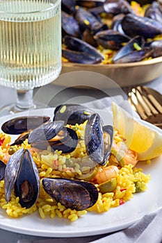 Paella with mussels and shrimps, on white plate, served with lemon and white wine, vertical