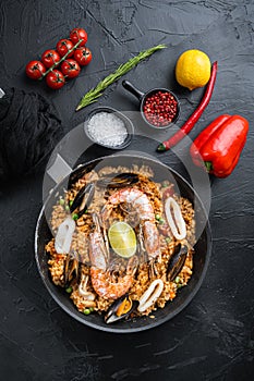 Paella traditional spanish dish served in frying pan, on black textured surface, top view