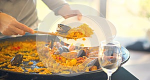 Paella. Traditional spanish food. Person putts seafood paella from the fry pan to plate. Paella with with mussels and squids photo