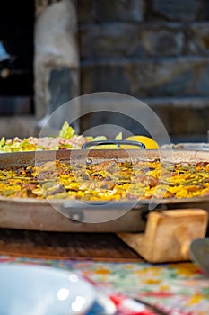 Paellera with a freshly cooked authentic Valencian paella, to serve on a table with the dishes set, salad, glasses and the photo