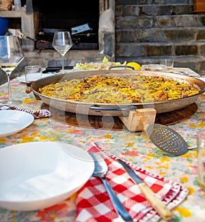 Paellera with a freshly cooked authentic Valencian paella, to serve on a table with the dishes set, salad, glasses and the floral photo