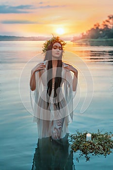 Pagan girl Slavic goddess emerges from water lake ritual flower wreaths float, candles burning. fashion model. Holiday