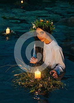 Pagan goddess. water lake, ritual flower wreaths float, candles burning. girl swims in riwer. white vintage shirt