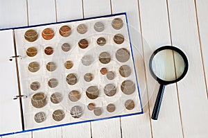 Page of numismatics album with different coins on a white wooden table