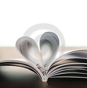 Pages of book curved into heart shape with couple wedding rings