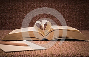 Pages of open book rolled in heart shape on table