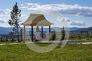 Pagoda with a bell in a Buddhist monastery on top of a mountain against a blue sky and green grass