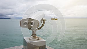 Paid observation point for the sea through binoculars, against a blurred background of the sea and a distant ship and sailboat