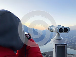 Paid outdoor tourist telescope. Girl in a red jacket taking pictures of the beautiful landscape