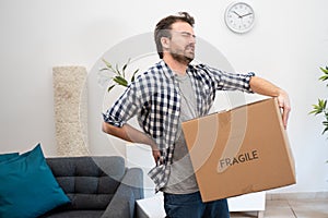 Pain in back. Young man suffering while lifting a cardboard box