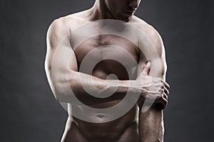 Pain in the elbow. Muscular male body. Handsome bodybuilder posing on gray background. Low key close up studio shot photo