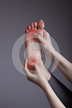 Pain in heel and ball of foot. Woman holding leg with red spot closeup. Inflammation, wearing wrong shoes, injuries