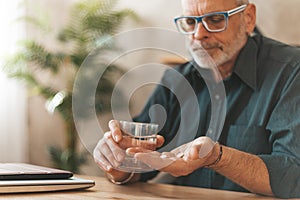 Pain medications. Senior man holding pills and a glass of water in his hands. Headache in the elderly