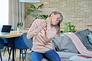 Pain in neck disturbing middle-aged woman, suffering female sitting at home