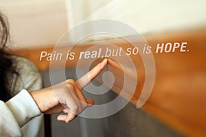 Pain is real, but so is HOPE. Young woman points her finger at positive inspirational text message on wooden wall background.