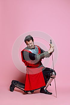 Crying young man, medieval warrior or knight wearing wearing armor clothing posing isolated over pink background