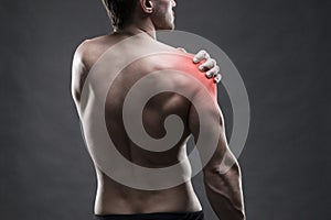 Pain in the shoulder. Muscular male body. Handsome bodybuilder posing on gray background. Low key close up studio shot