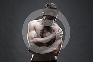 Pain in the shoulder. Muscular male body. Handsome bodybuilder posing on gray background. Low key close up studio shot photo