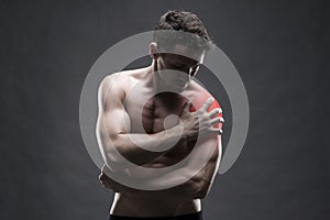 Pain in the shoulder. Muscular male body. Handsome bodybuilder posing on gray background