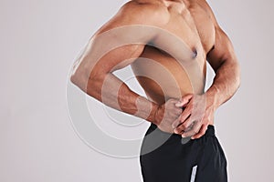 Pain, waist and man with an injury after exercise, fitness and training against a grey studio background. Healthcare