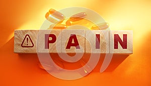 Pain word with oil capsules around on orange background. Medical healthcare concept