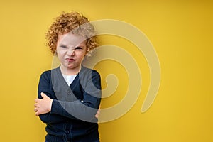 pained child boy with arms folded posing at camera, isolated on yellow in studio