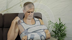 Painful, bored man with a broken arm wearing arm brace sitting on a sofa