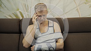 Painful, bored man with a broken arm wearing arm brace sitting on a sofa