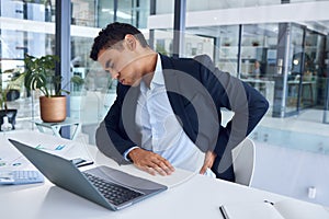 The pains of working long hours. Shot of a young businessman experiencing back pain while working in an office.