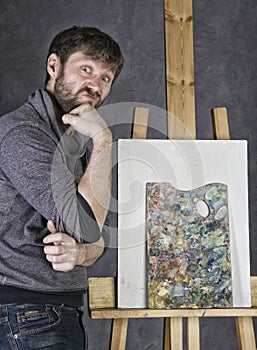 Paint artist posing next to a canvas and contemplating, depicts a reverie