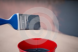 Paint brush and a bucket with paint next to a building exterior wall. Painting house plinth outside. Home renovation. Nobody