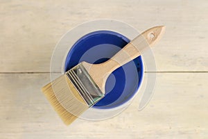 A paint brush is lying on the blue lid of a plastic paint bucket on an old white vintage wooden plank table. Place for text or