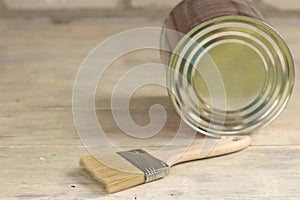 A paint brush is next to a metal can on an old white vintage wooden plank table. Brick wall in the background. Place for text or