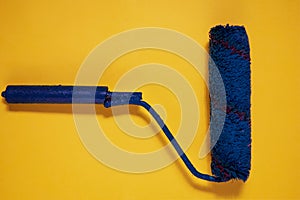 Paint brush roller on yellow background. Blue used paint tool as a concept of refurbishing, re branding and changes. Mock-up color photo