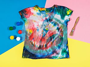 Paint, brush, and tie dye t-shirt on a three-color background. Flat lay.