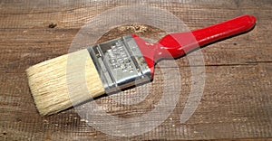 Paint brush width 2 inch with a red handle on a wooden background