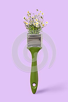 Paint brush with wildflowers chamomile on a violet background, copy space. Painting summer landscape.