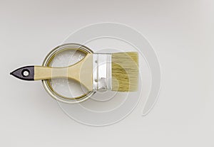 Paint brush with a wooden handle on a can of white paint, top view. Light background, free space for text